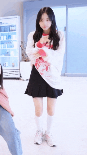 a girl wearing a white sweater and a black skirt stands in front of a refrigerator