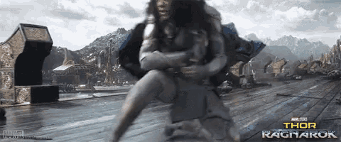 a woman is kneeling down next to a man in a movie scene from thor ragnarok .