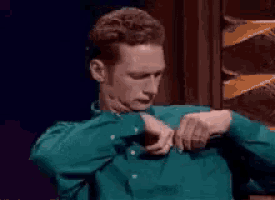 a man in a green shirt is taking off his shirt and looking at his watch .