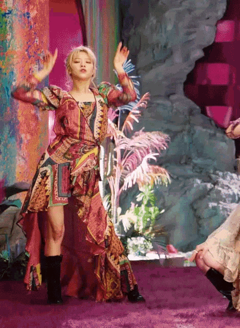 a woman in a colorful dress is dancing in front of a pink wall