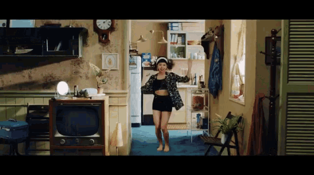 a woman is dancing in a kitchen with a clock on the wall