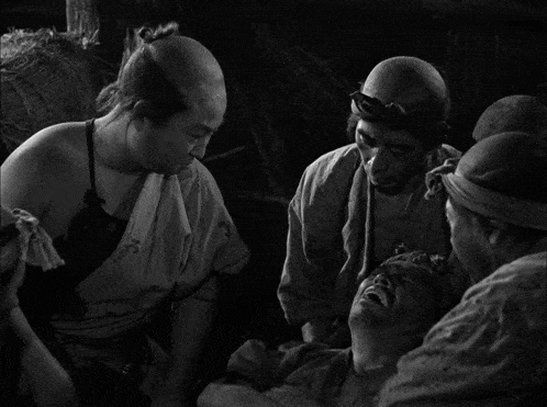 a group of men are gathered around a man with a bandaged head