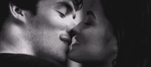 it is a black and white photo of a man and woman kissing .
