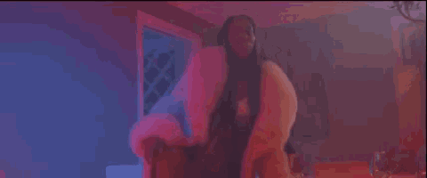 a woman in a fur coat is sitting in a chair in a room in a pink light .