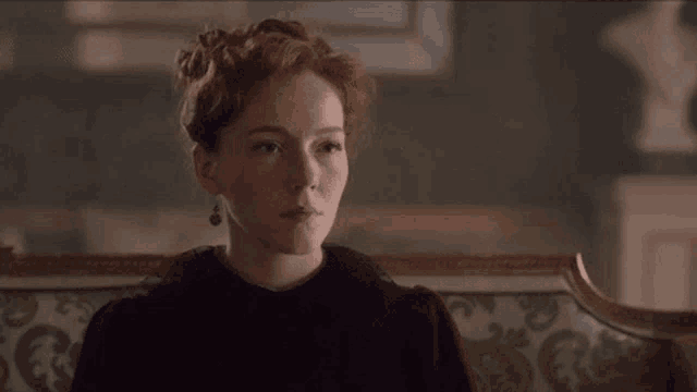 a woman with red hair is sitting on a couch in a room looking up .