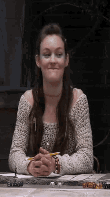 a woman is sitting at a table with her hands folded and a pencil .