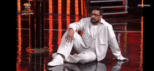 a man in a white suit and glasses is sitting on a stage .