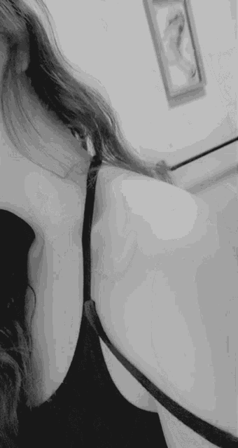 a woman in a black bra is taking a selfie in a bathroom in a black and white photo .