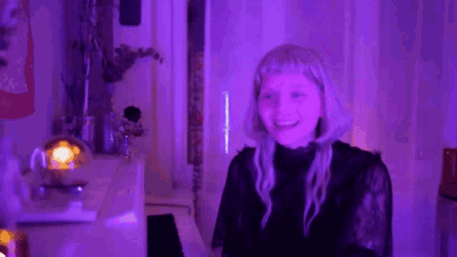 a woman in a black dress is dancing in a room with purple light .