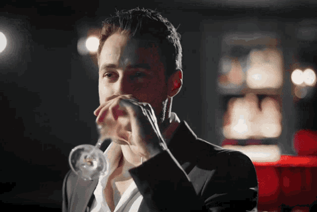 a man in a tuxedo is drinking from a wine glass
