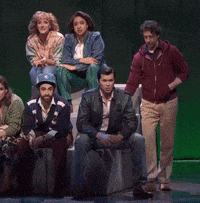 a group of people are standing and sitting on a stage in front of a green background