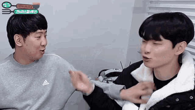 a man wearing a grey adidas sweatshirt is talking to another man