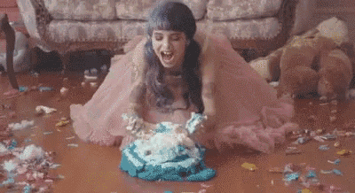 a woman in a pink dress is sitting on the floor with a cake in her hands .
