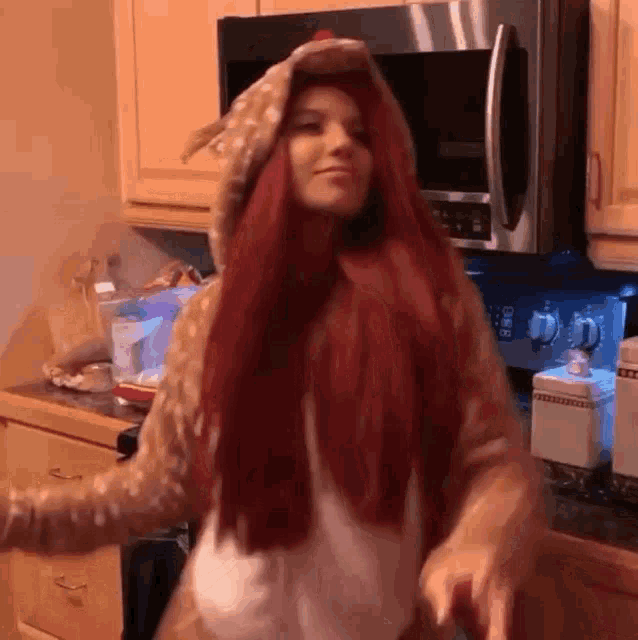 a woman with red hair is dancing in a kitchen in front of a stainless steel microwave .