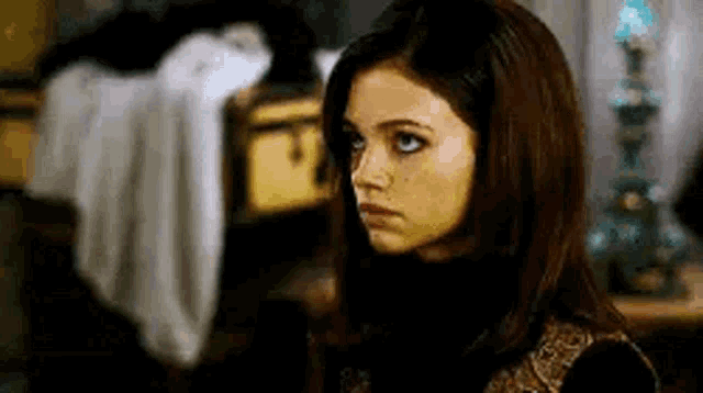 a woman with long brown hair and blue eyes is standing in a room looking at the camera .