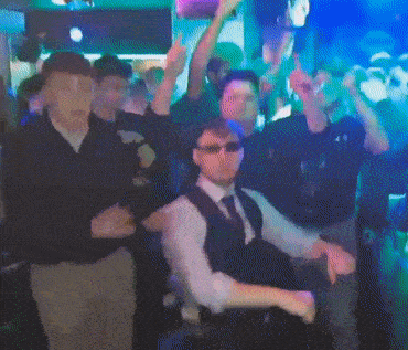 a group of men are dancing in a dark room with their hands in the air