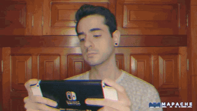 a man holding a nintendo switch in front of a wall