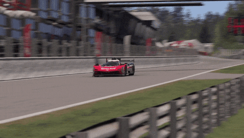 a red race car is driving on a track with a fence behind it