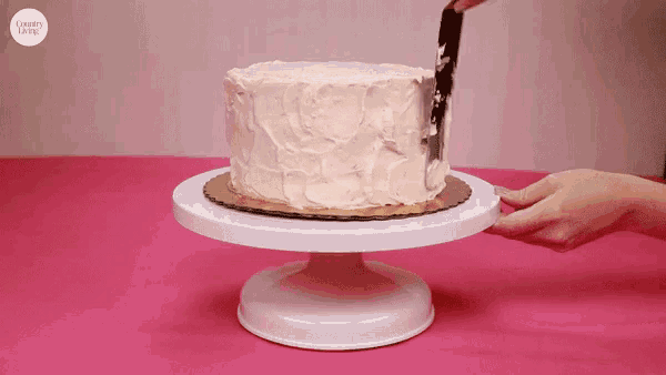 a person is frosting a cake on a cake stand with a knife .