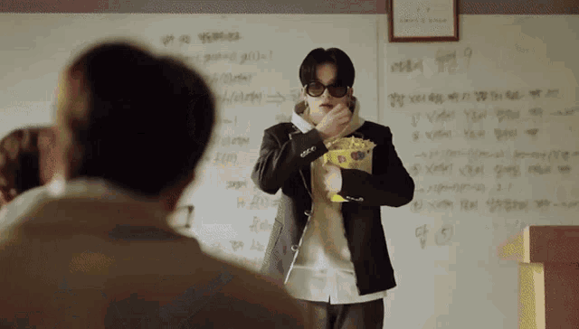 a man holding a bag of popcorn in front of a white board with numbers on it