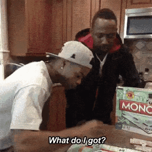 two men are playing monopoly in a kitchen and one of them is asking the other what do i got