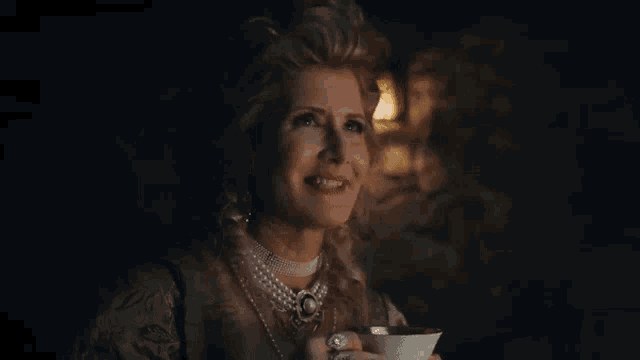a woman in a pearl necklace is holding a cup of coffee