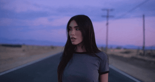 a woman in a gray shirt is standing in the middle of the road