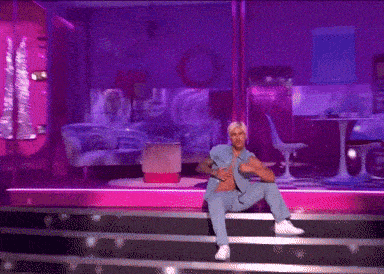 a man in a blue shirt is sitting on a stage in front of a coca cola sign
