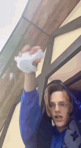 a young man wearing glasses and a blue hoodie is holding a piece of paper in his hand .