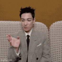 a man in a suit and tie is sitting on a couch making a funny face .