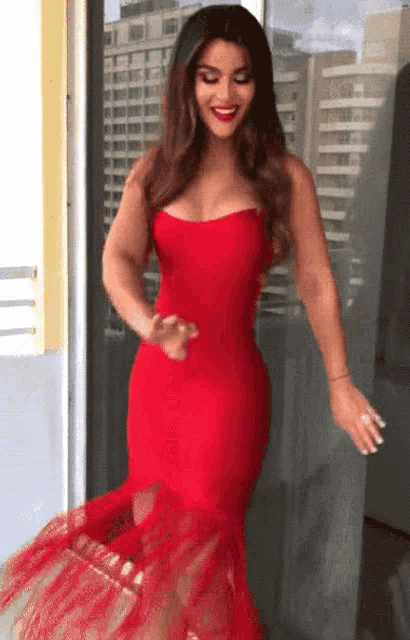 a woman in a red dress is standing in front of a building