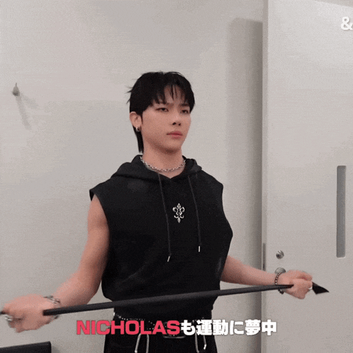a man in a black sleeveless hoodie is holding a bar with nicholas written in red