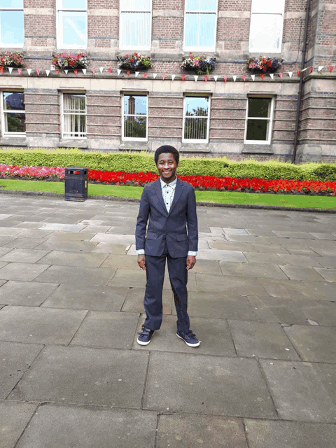 a young boy in a suit stands in front of a large building
