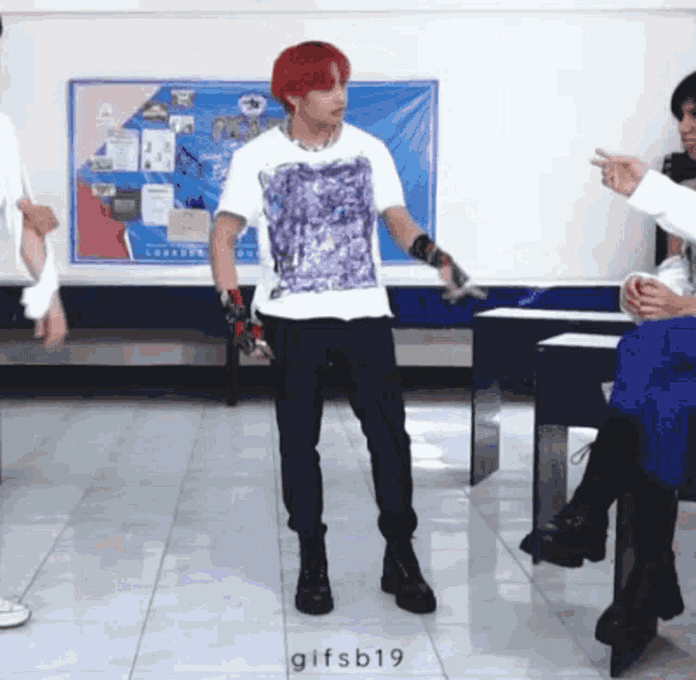 a man with red hair is dancing in front of a group of people in a classroom .