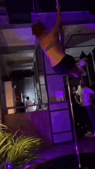 a woman is standing on a pole in a dark room with purple lights .