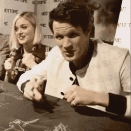 a man and a woman are sitting at a table signing autographs for fans .