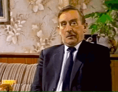 a man in a suit and tie is sitting on a couch looking at the camera