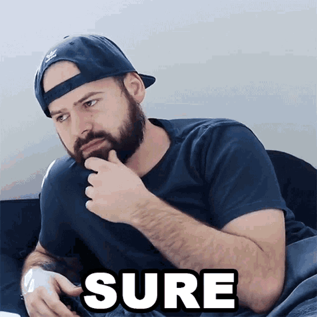 a man with a beard wearing a hat and a t-shirt that says sure on it