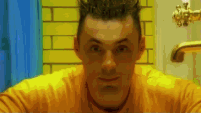 a man in a yellow shirt is looking at himself in a bathroom mirror
