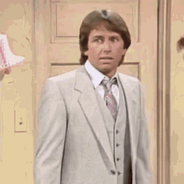 a man in a suit and tie is standing in front of a door and looking at something .