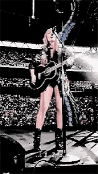 a woman is singing into a microphone while holding a guitar on stage .