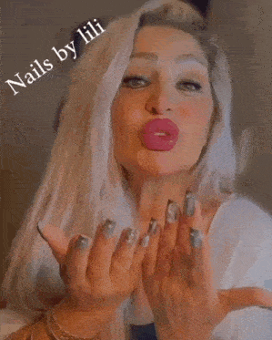 a woman with long white hair and gray nails is smiling while holding her hands together .