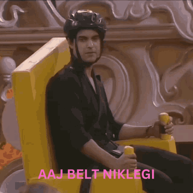 a man wearing a helmet is sitting in a yellow chair with the words aaj belt nikleji written on the bottom