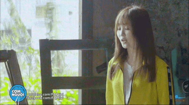 a girl in a yellow jacket stands in front of a window
