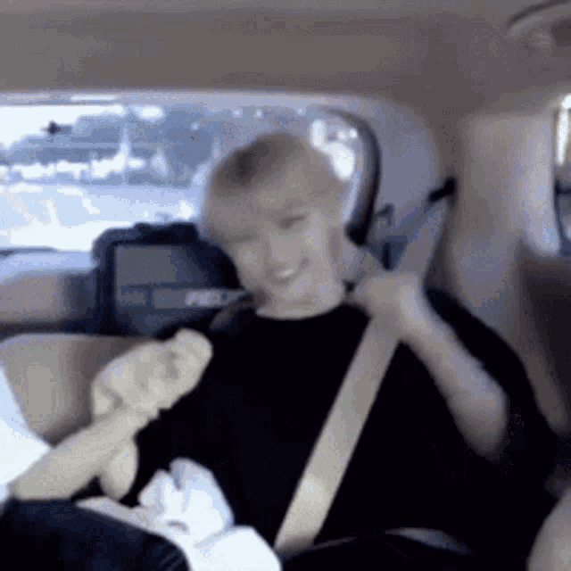 a man in a black shirt is sitting in the back seat of a car adjusting his seat belt .