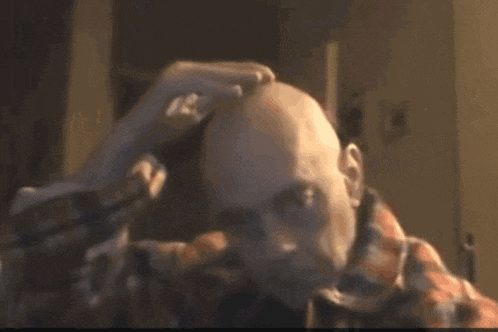 a man in a plaid shirt is shaving his head with a razor