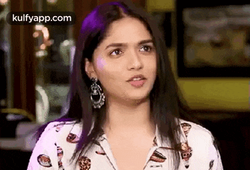 a young woman wearing a white shirt and earrings is making a funny face .