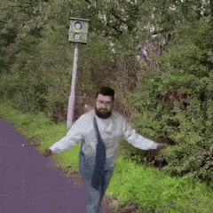 a man with a beard and glasses is walking down a path next to a traffic light