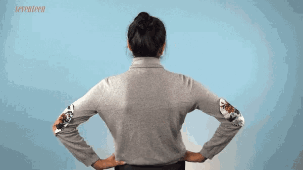 a woman is standing with her hands on her hips wearing a grey sweater with floral sleeves .