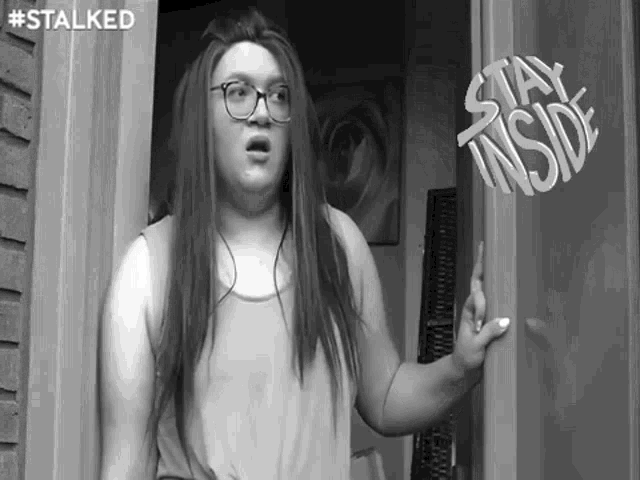 a black and white photo of a woman standing in front of a door with the words stay inside written on it